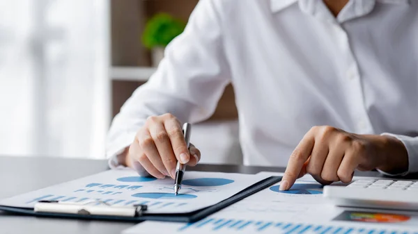 Close-up businesswoman's hand holding a pen pointing at a bar chart on a corporate financial information sheet, the businesswoman examines the financial information provided by the finance department.