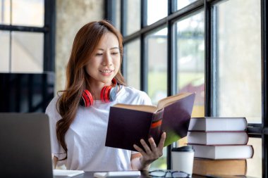Asyalı bir kız öğrenci dizüstü bilgisayar kullanıyor. İnternette çalışıyor. Bilgisayara dikkatlice bakıyor ve öğretmenin öğrettiklerini dinliyor. Çevrimiçi öğrenme kavramı.