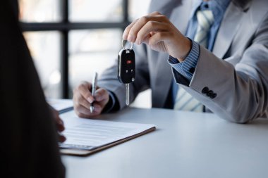 The car salesman hands the key to the customer after discussing the details and signing the purchase agreement, selling the car, selling the car from a major dealer. Vehicle sales concept.