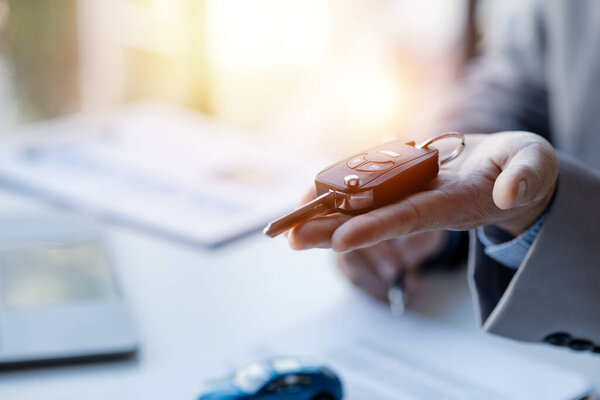 The salesman puts it on his hand to hand it to the customer after explaining the details and agreeing to sign the contract, sells cars, sells cars at major dealers. Vehicle sales concept.