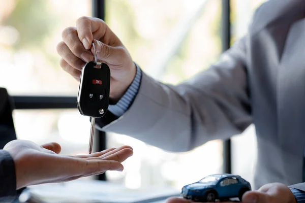 The car salesman hands the key to the customer after discussing the details and signing the purchase agreement, selling the car, selling the car from a major dealer. Vehicle sales concept.