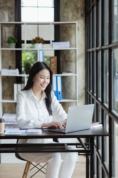 An Asian female employee sits in the office of the marketing department of a startup company, she is a marketing, customer liaison and consulting worker. Marketing concept.