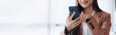 Businesswoman looking at financial information from a mobile phone, she is checking company financial documents, she is a female executive of a startup company. Concept of financial management.
