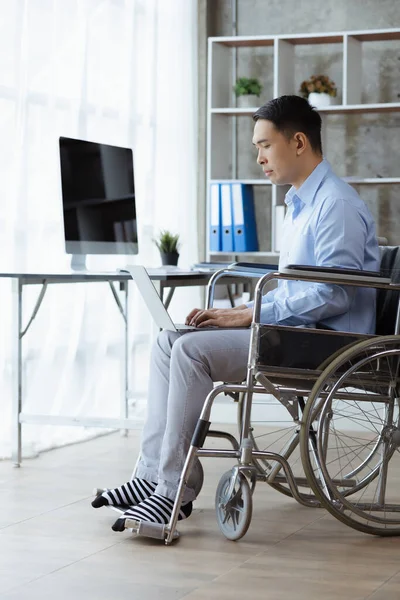 A man sits in a wheelchair, a man with a disability is in a wheelchair and works in the company office, working with the company team and having a disabled person as part of the team.