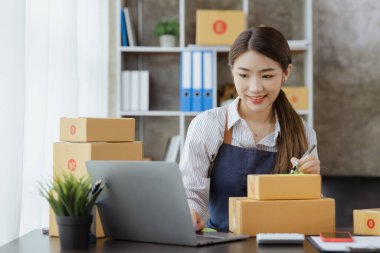 Bir e-ticaret şirketini işleten kadın, onlara göndermeden önce müşterilerin bir listesini kağıda yazıyor. Web sitelerinde ve sosyal medyada bir e-ticaret şirketi işletiyor. Çevrimiçi ürün satma kavramı.