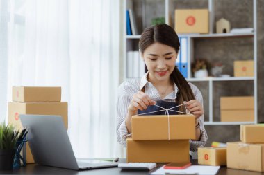 Paketi müşteri kutusuna bağlayan Asyalı bir kadın, çevrimiçi bir mağazası var, özel bir nakliye şirketi aracılığıyla paketleyip gönderiyor. Çevrimiçi satış ve online alışveriş kavramları.