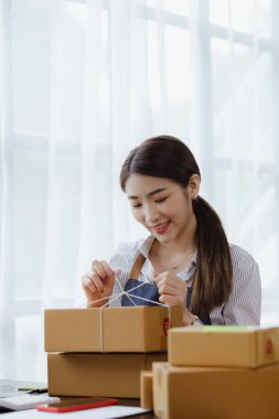 Paketi müşteri kutusuna bağlayan Asyalı bir kadın, çevrimiçi bir mağazası var, özel bir nakliye şirketi aracılığıyla paketleyip gönderiyor. Çevrimiçi satış ve online alışveriş kavramları.