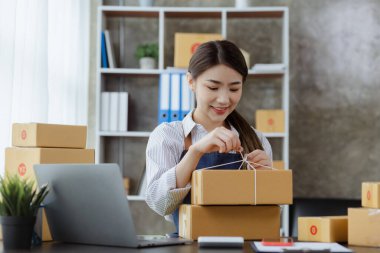 Paketi müşteri kutusuna bağlayan Asyalı bir kadın, çevrimiçi bir mağazası var, özel bir nakliye şirketi aracılığıyla paketleyip gönderiyor. Çevrimiçi satış ve online alışveriş kavramları.