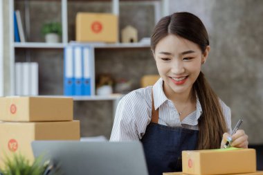 Bir e-ticaret şirketini işleten kadın, onlara göndermeden önce müşterilerin bir listesini kağıda yazıyor. Web sitelerinde ve sosyal medyada bir e-ticaret şirketi işletiyor. Çevrimiçi ürün satma kavramı.
