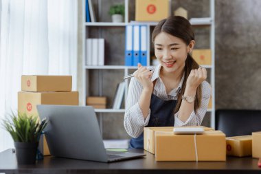 Güzel bir Asyalı işletme sahibi online bir dükkan açıyor, müşterilerin siparişlerini kontrol ediyor, bir kurye şirketi aracılığıyla mal gönderiyor, bir kadının online iş kurma kavramı.