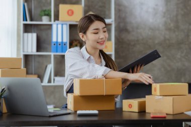 Online mağazası olan bir kadın müşterilere teslim edilecek paketleri sayıyor, internetten satıyor ve özel bir nakliye şirketi aracılığıyla paketliyor. Bir kadının online iş kurma kavramı.
