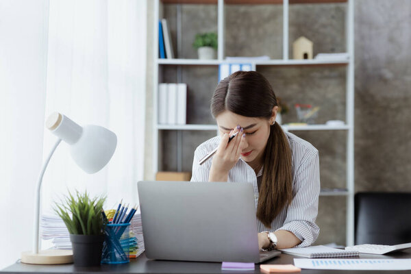 Beautiful Asian woman working in an office, she is a businesswoman who owns a company, she has a headache due to long and large paperwork leaving her tired and dizzy. The concept of sickness from work