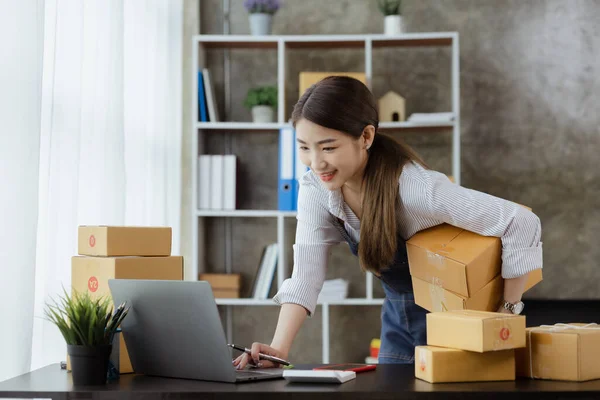 A beautiful Asian business owner opens an online store, she is checking orders from customers, sending goods through a courier company, concept of a woman opening an online business.
