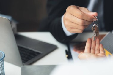 Bir ev kiralama şirketi çalışanı kira sözleşmesi imzalamayı kabul eden bir müşteriye kira sözleşmesinin detaylarını ve şartlarını açıklayan ev anahtarlarını teslim ediyor. Ev ve gayrimenkul kiralama fikirleri.