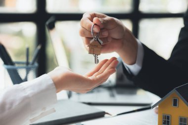 A home rental company employee is handing the house keys to a customer who has agreed to sign a rental contract, explaining the details and terms of the rental. Home and real estate rental ideas.