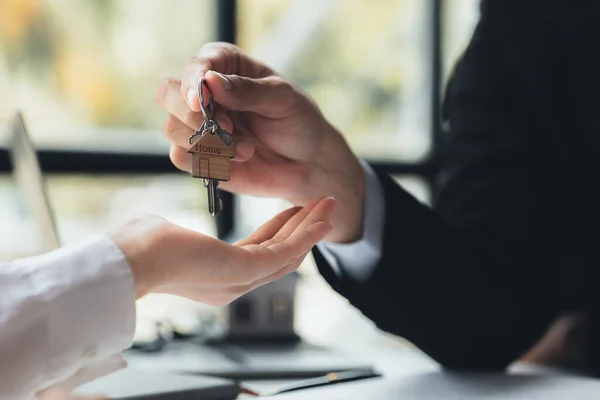 A home rental company employee is handing the house keys to a customer who has agreed to sign a rental contract, explaining the details and terms of the rental. Home and real estate rental ideas.