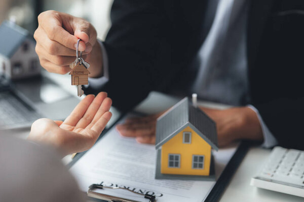 A home rental company employee is handing the house keys to a customer who has agreed to sign a rental contract, explaining the details and terms of the rental. Home and real estate rental ideas.