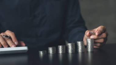 Business man putting a coin on a pile of coins. Placing coins in a row from low to high is comparable to saving money to grow more. The concept of growing savings and saving by investing in stock