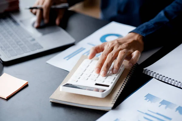 Businessman is using a calculator to calculate company financial figures from earnings papers, a businessman sitting in his office where the company financial chart is placed. Banner with copy space.