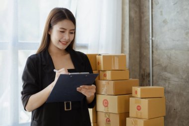 Bir çevrimiçi mağazanın sahibi, paketlenmiş ürünlerin siparişlerini web sitesinden sipariş edildiği gibi müşterilere teslimata hazırlamak için kontrol etmektedir. Çevrimiçi satış ve online alışveriş kavramları.