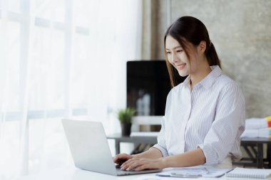 A beautiful Asian businesswoman sitting in her private office, she is checking company financial documents, she is a female executive of a startup company. Concept of financial management.