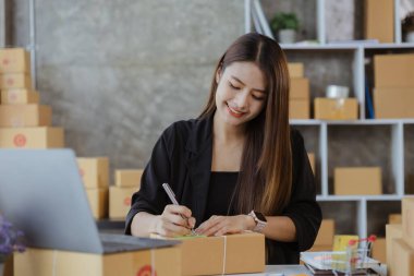 Woman who runs an e-commerce business is writing a list of customers on paper before shipping to them, she runs an e-commerce business on websites and social media. Concept of selling products online.