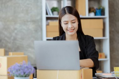 Güzel bir Asyalı işletme sahibi online bir dükkan açıyor, müşterilerin siparişlerini kontrol ediyor, bir kurye şirketi aracılığıyla mal gönderiyor, bir kadının online iş kurma kavramı.