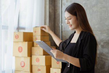 Bir çevrimiçi mağazanın sahibi, paketlenmiş ürünlerin siparişlerini web sitesinden sipariş edildiği gibi müşterilere teslimata hazırlamak için kontrol etmektedir. Çevrimiçi satış ve online alışveriş kavramları.