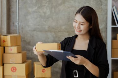 Bir çevrimiçi mağazanın sahibi, paketlenmiş ürünlerin siparişlerini web sitesinden sipariş edildiği gibi müşterilere teslimata hazırlamak için kontrol etmektedir. Çevrimiçi satış ve online alışveriş kavramları.