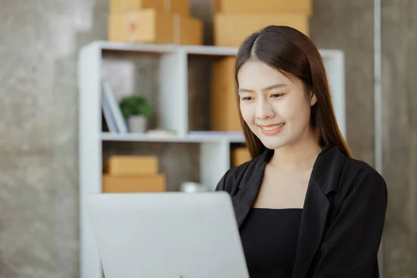 A beautiful Asian business owner opens an online store, she is checking orders from customers, sending goods through a courier company, concept of a woman opening an online business.