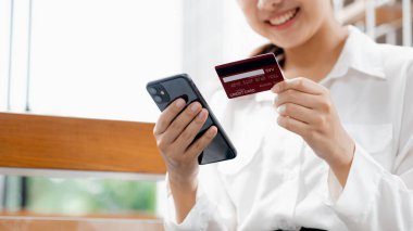 Asian woman holding smartphone and credit card, she is shopping online on smartphone through online shopping app and paying for goods and services via credit card. Online shopping concept.