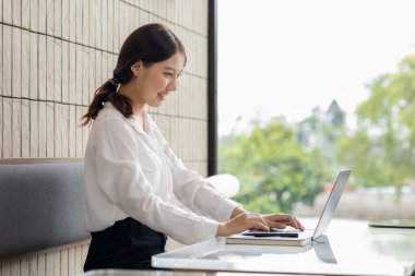 Asian woman working on laptop, female employee of a marketing company, she is working on a marketing plan for a company to generate income and profit, grow sales. Marketing planning concept.