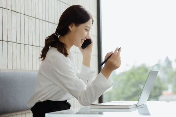 Asian woman talking on the phone on the sofa in her private office, young businesswoman founding startup company, running business by young female executives, business concept and led by female boss.