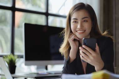 Asian businesswoman looking at smartphone screen and remote video call with startup partner, she talks to her friend through program on smartphone. Concept of using communication technology.