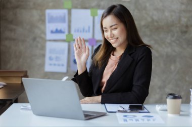 Beautiful Asian businesswoman sitting in her private office, she is talking to her partner via video call on her laptop, she is a female executive of a startup company. Concept of financial management