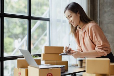 Bir çevrimiçi mağazanın sahibi, paketlenmiş ürünlerin siparişlerini web sitesinden sipariş edildiği gibi müşterilere teslimata hazırlamak için kontrol etmektedir. Çevrimiçi satış ve online alışveriş kavramları.