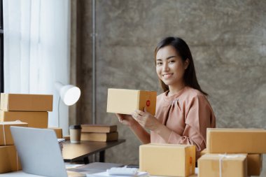 Bir çevrimiçi mağazanın sahibi, paketlenmiş ürünlerin siparişlerini web sitesinden sipariş edildiği gibi müşterilere teslimata hazırlamak için kontrol etmektedir. Çevrimiçi satış ve online alışveriş kavramları.
