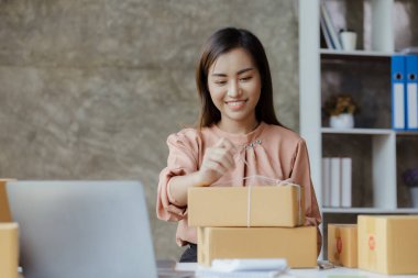 Paketi müşteri kutusuna bağlayan Asyalı bir kadın, çevrimiçi bir mağazası var, özel bir nakliye şirketi aracılığıyla paketleyip gönderiyor. Çevrimiçi satış ve online alışveriş kavramları.