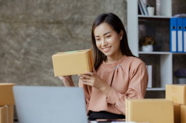 Bir çevrimiçi mağazanın sahibi, paketlenmiş ürünlerin siparişlerini web sitesinden sipariş edildiği gibi müşterilere teslimata hazırlamak için kontrol etmektedir. Çevrimiçi satış ve online alışveriş kavramları.