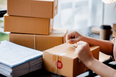 Paketi müşteri kutusuna bağlayan Asyalı bir kadın, çevrimiçi bir mağazası var, özel bir nakliye şirketi aracılığıyla paketleyip gönderiyor. Çevrimiçi satış ve online alışveriş kavramları.