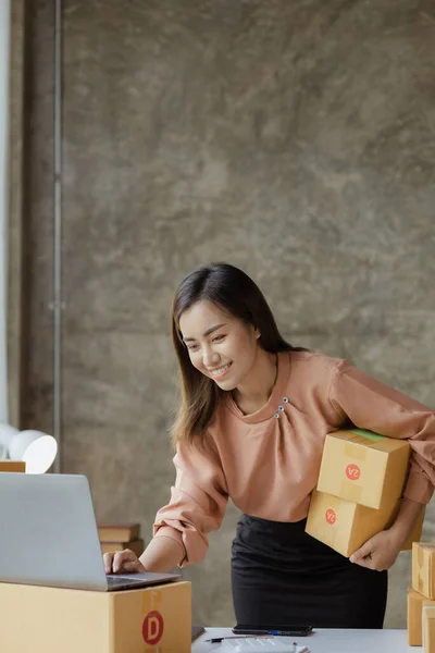 A beautiful Asian business owner opens an online store, she is checking orders from customers, sending goods through a courier company, concept of a woman opening an online business.