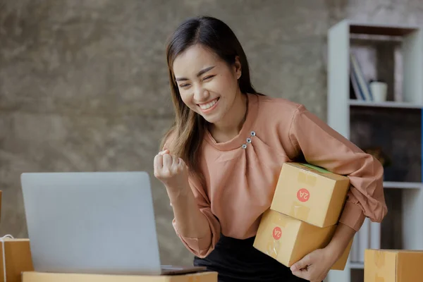 Woman who runs an online store with a happy face is to check sales, she sells online and packs goods through a private shipping company. concept of a woman opening an online business