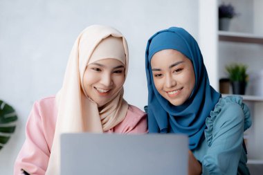 Two hijab-clad Asian women are brainstorming together in a conference room for a startup, run by a young, talented woman. The management concept runs the company of female leaders to grow the company.