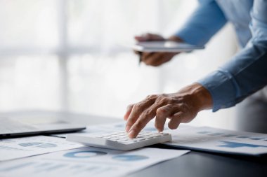 Businessman is using a calculator to calculate company financial figures from earnings papers, a businessman sitting in his office where the company financial chart is placed. Banner with copy space.