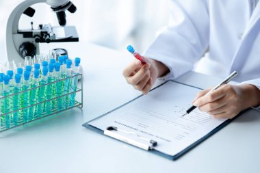 Bir laboratuvar asistanı, bir tıp bilimcisi, bir kimya araştırmacısı bir test tüpü tutuyor ve bir hastanın kan örneğinden hastalığı inceliyor. Tıp ve araştırma konsepti.