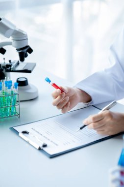 Bir laboratuvar asistanı, bir tıp bilimcisi, bir kimya araştırmacısı bir test tüpü tutuyor ve bir hastanın kan örneğinden hastalığı inceliyor. Tıp ve araştırma konsepti.