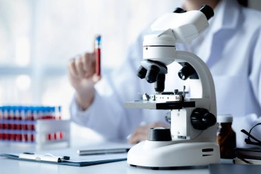 Microscope in lab of the Pharmaceutical Research Center, a chemistry researcher holds a test tube of chemicals and examines the disease from a patient's blood sample. Medicine and research concept.