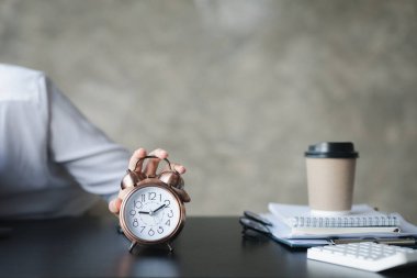 A person's hand presses the desk clock to turn off the alarm, he is lying down during a break during work hours to relax. The idea of taking a break during the working day.