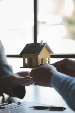 Konut satıcısının elinde bir ev modeli var ve onu müşterilere örnek bir ev projesi olarak sunuyor. Satıcının müşterilere öğüt verdiği bir ev. Projede ev satma kavramı.