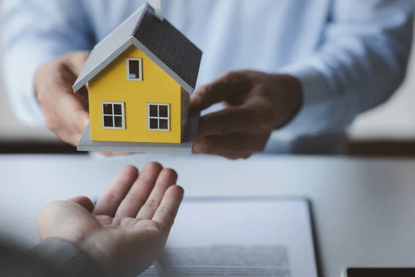 A housing salesman holds a model of a house and sends it to customers as an example, a sample house project where a salesperson advises customers. The concept of selling houses in the project.